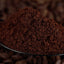ground Cafe Brasileiro Tradicional coffee in black spoon and coffee beans on background