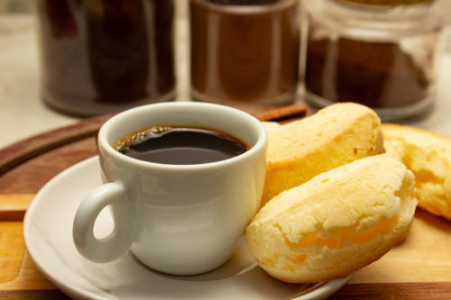 Cup of café do ponto brazilian coffee with pao de queijo on a wooden board