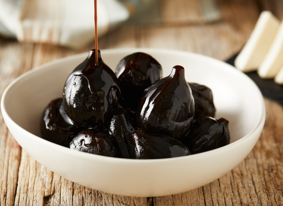 White bowl on wood table with figs with heavy syrup being poured on them