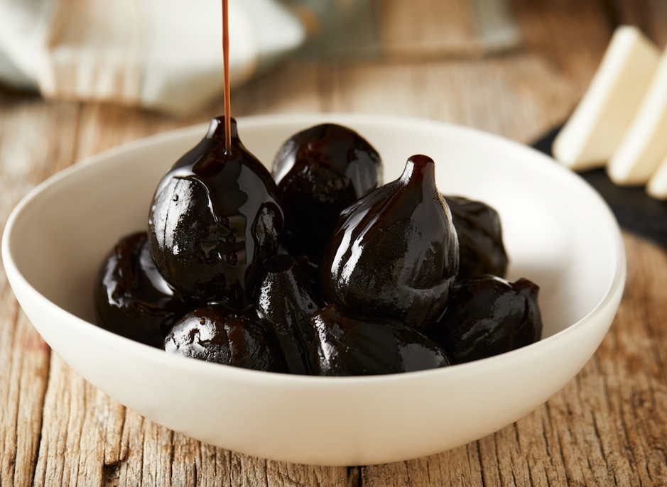 White bowl on wood table with figs with heavy syrup being poured on them 