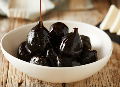 White bowl on wood table with figs with heavy syrup being poured on them