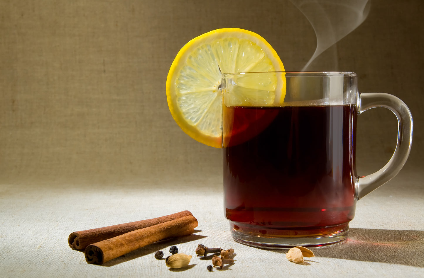 glass mug with té, canela y clavo with lemon slice, cinnamon and cloves on table 