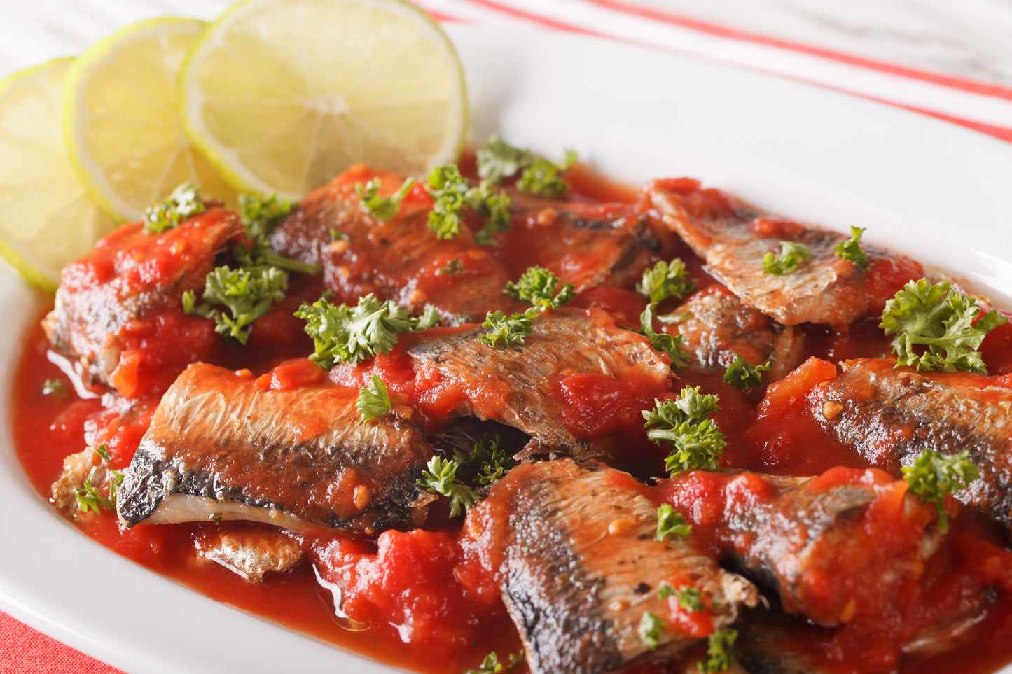 Sardines in spicy tomato sauce on white plate with lemon