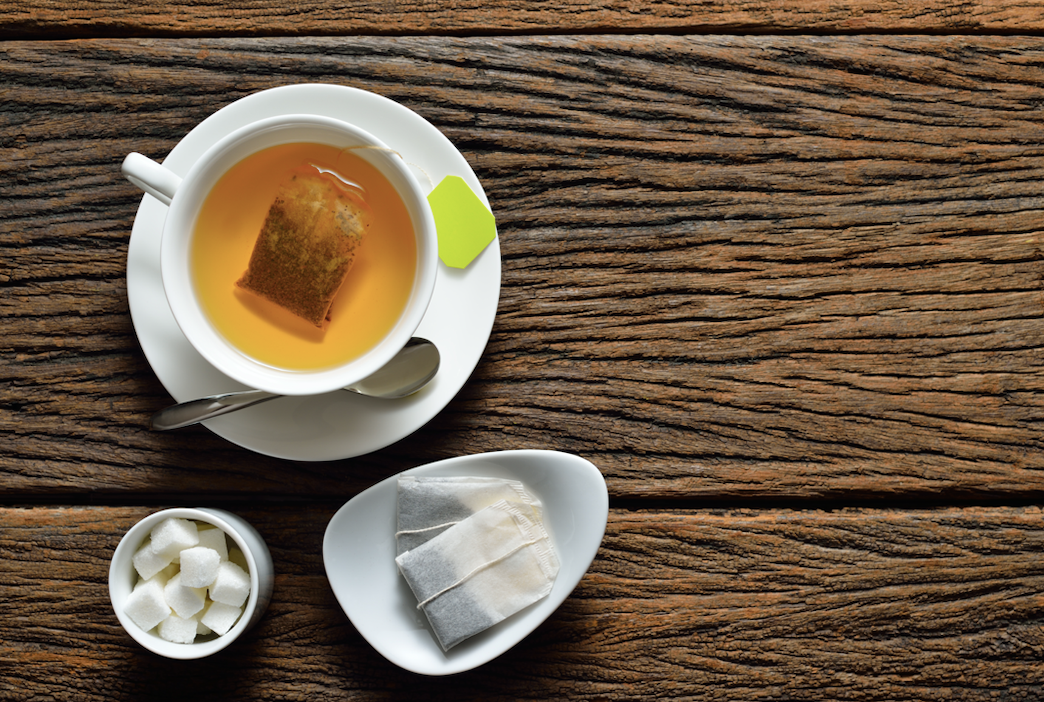 cup of tea with tea bag and sugar cube on wooden table