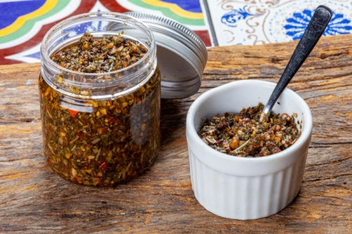 Jar of chimichurri made with adobo seasoning and white bowl and spoon