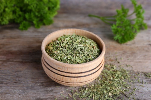 Bowl with dry parsley on wooden table